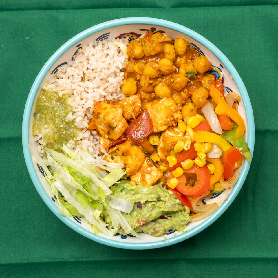 Colorful burrito bowl with rice, chickpeas, chicken, peppers, corn, guacamole, and lettuce.