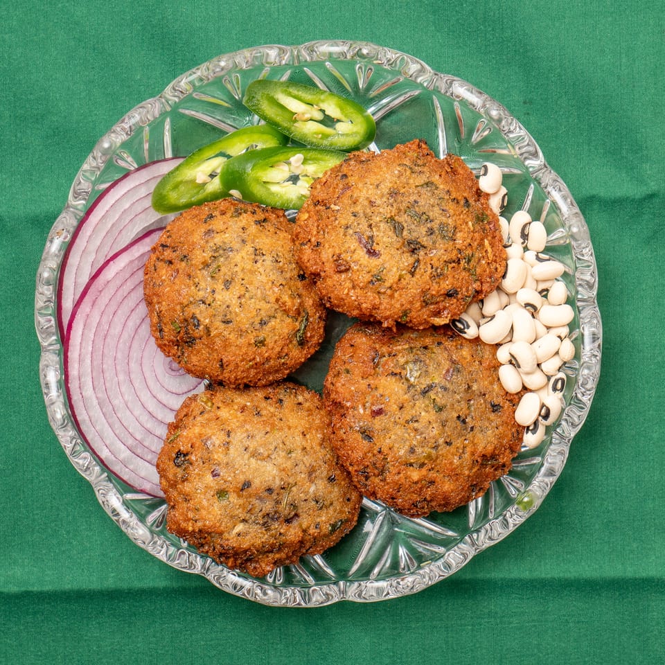 Four golden-brown falafel patties on a glass plate with red onion, jalapeños, and black-eyed peas.