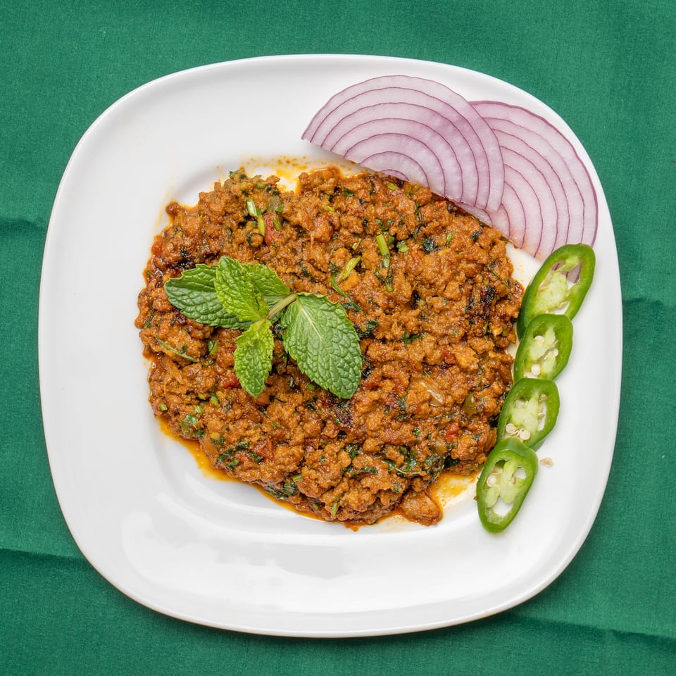 Spicy keema curry garnished with mint, red onion slices, and green chilies on a white plate.